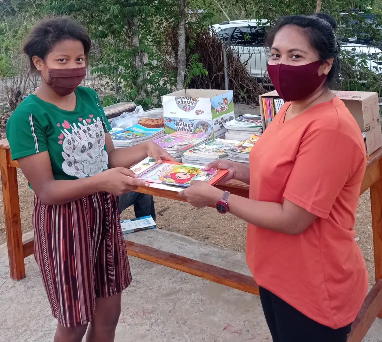 Dince Abanat handing out one of the first books from the LBAT library to a young student.