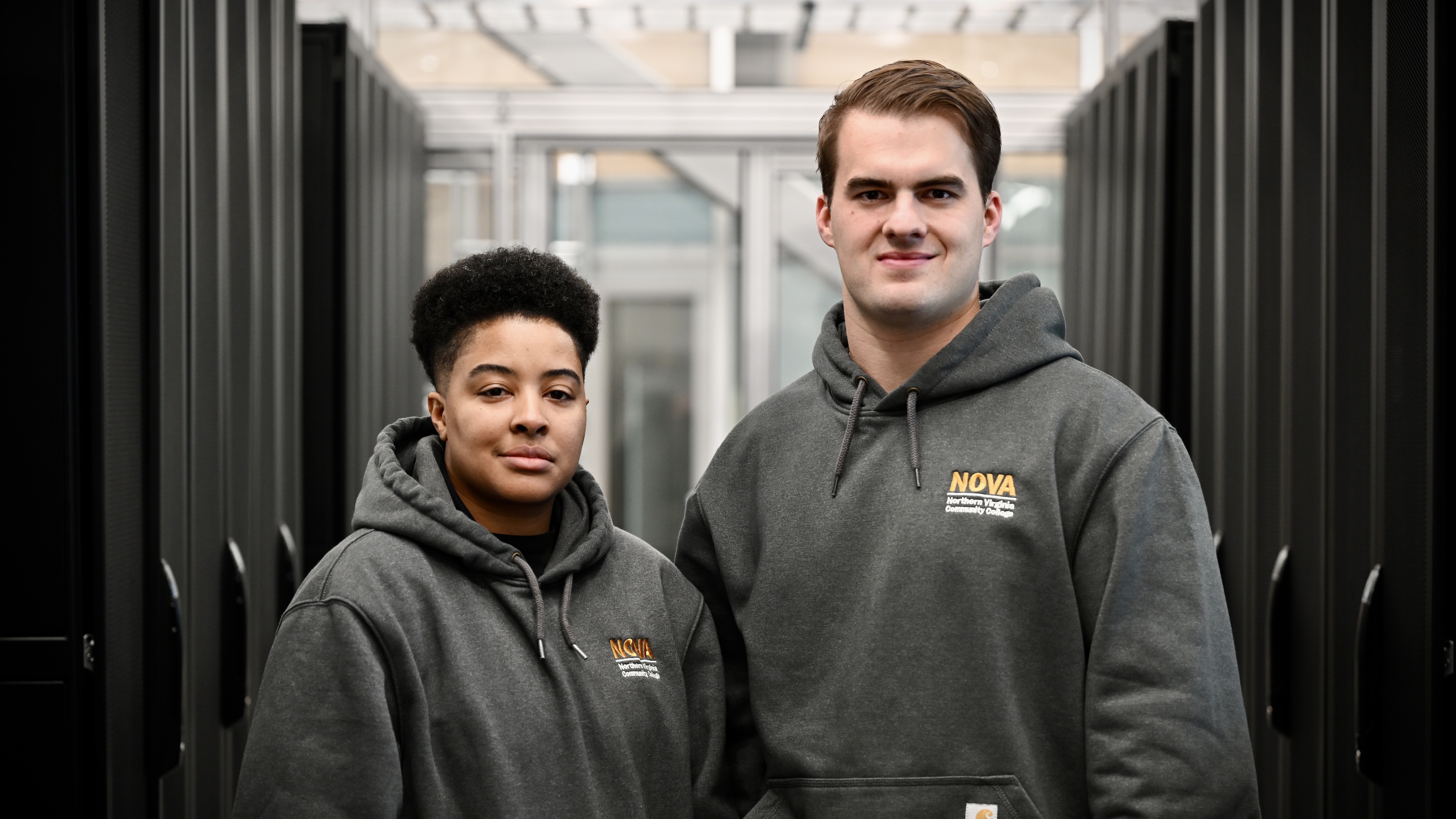 A photo of 2 active-duty military members who are also NOVA students in AWS’ Skillbridge Program. They are standing in between rack housing units at NOVA’s Data Center Training Facility.