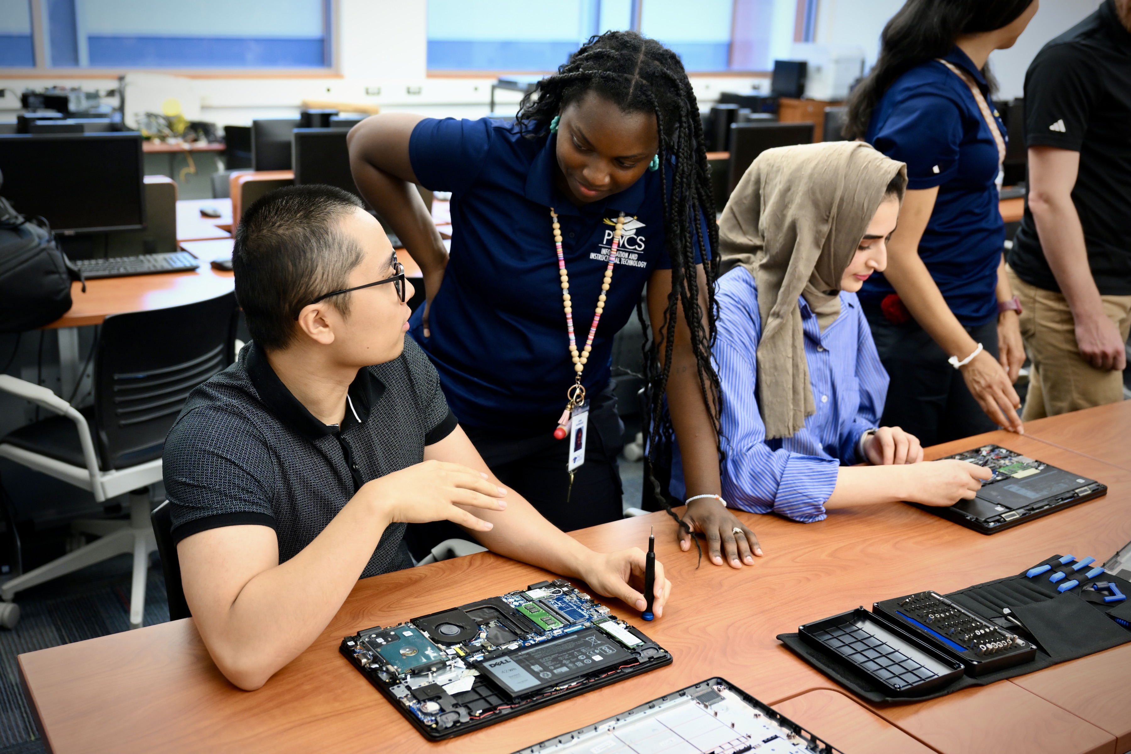 A supervisor for Prince William County Schools (PWCS) speaks with an IT intern while they refurbish a laptop.